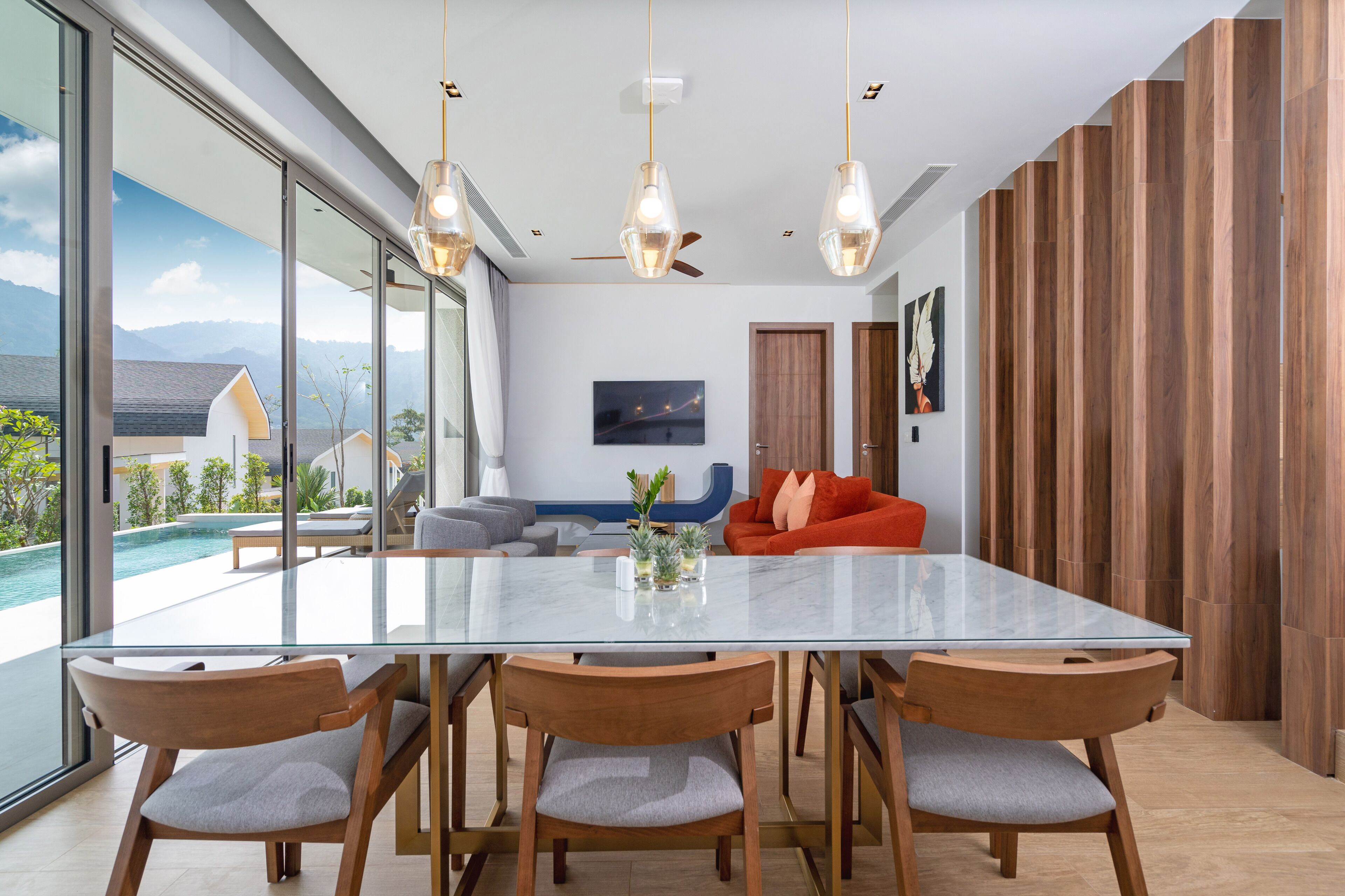 A modern dining area with a glass table, wooden chairs, and pendant lights.