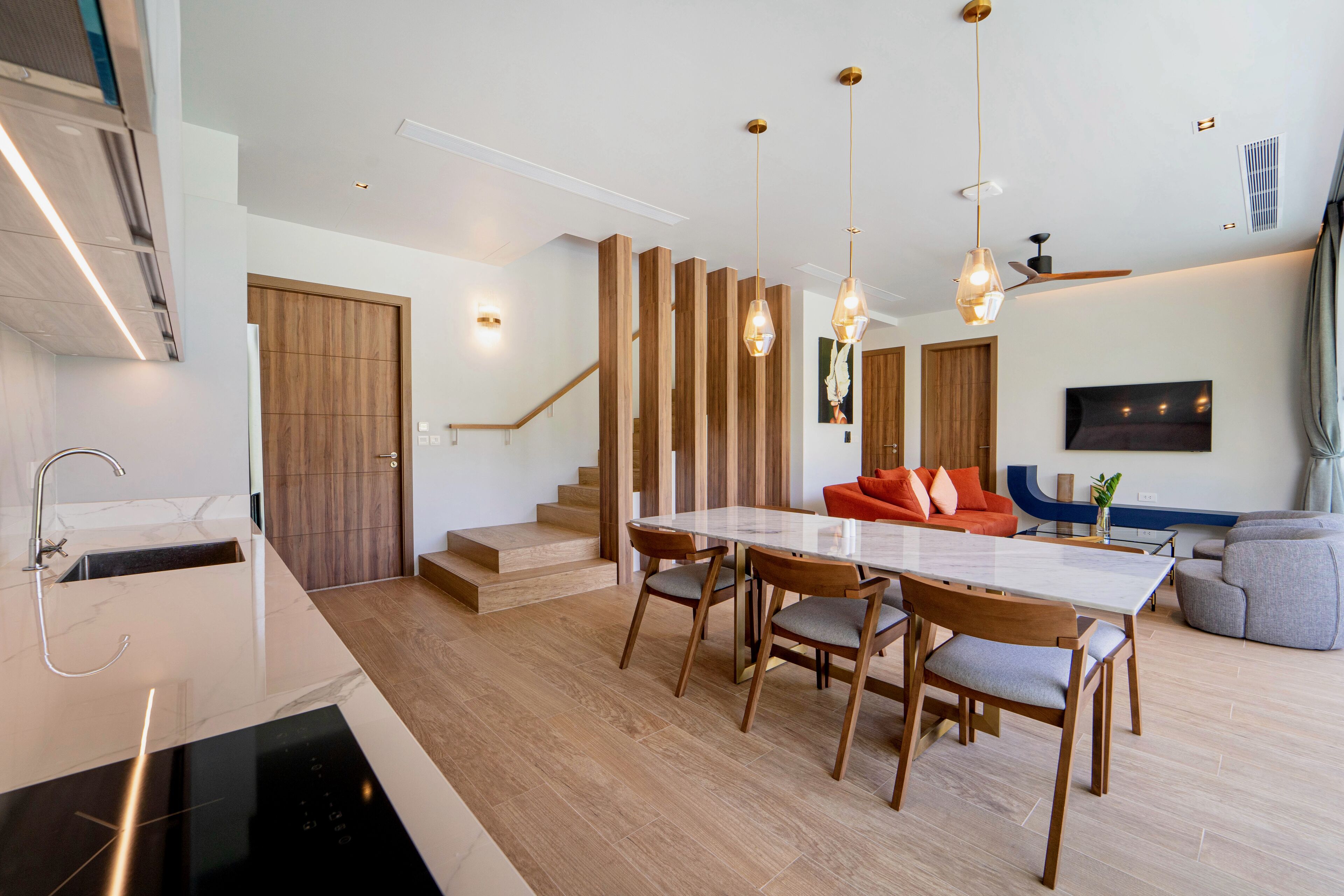 A modern kitchen with a built-in dishwasher, a dining area with a large table and chairs, and a staircase leading to an upper level.