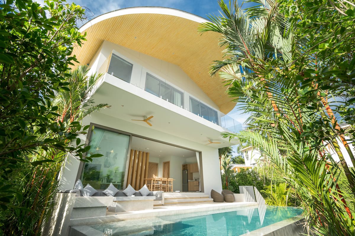 Une maison moderne à deux étages, dotée d’une piscine, de grandes fenêtres et d’un toit incurvé.