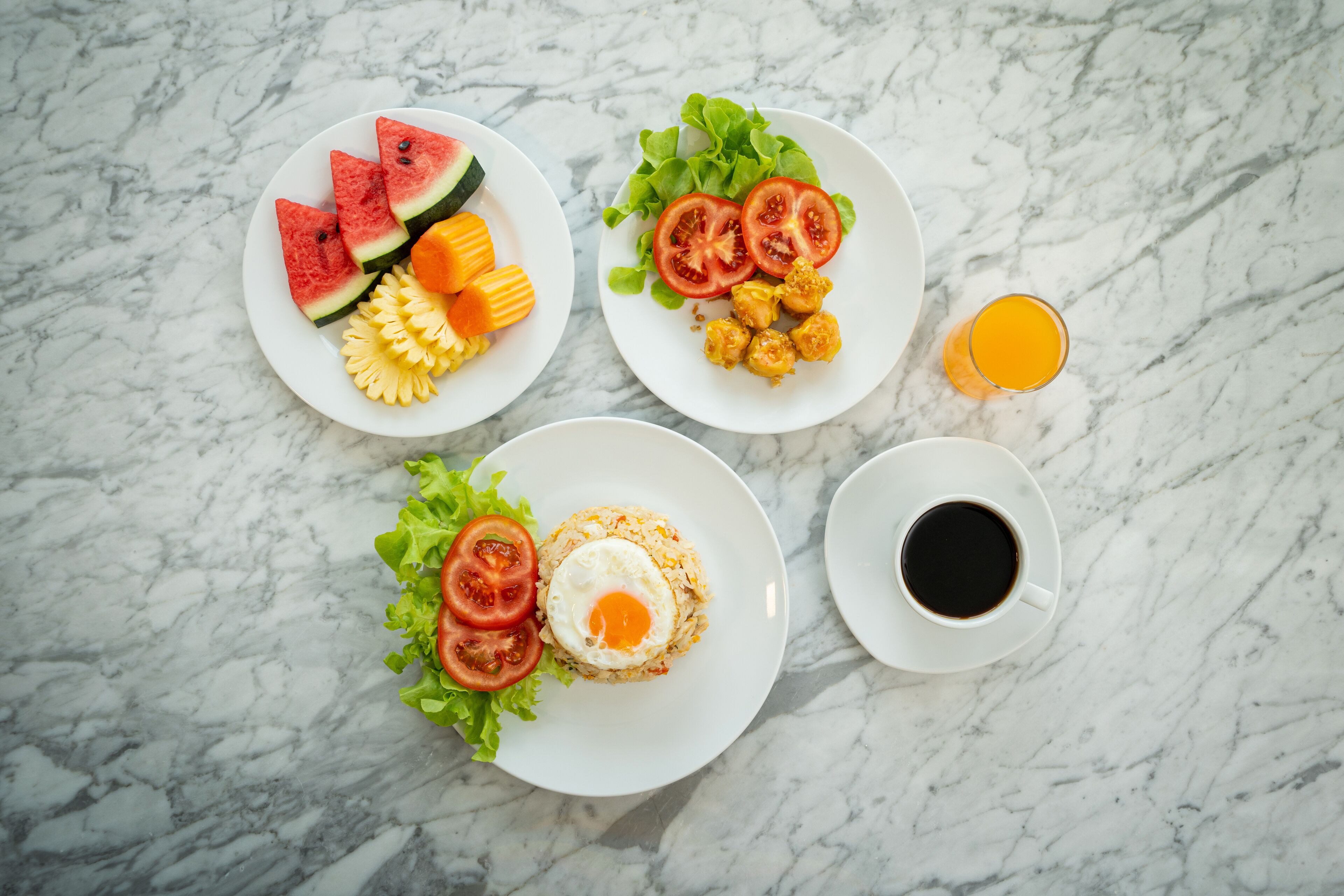Three plates of food and a cup of coffee on a marble surface.