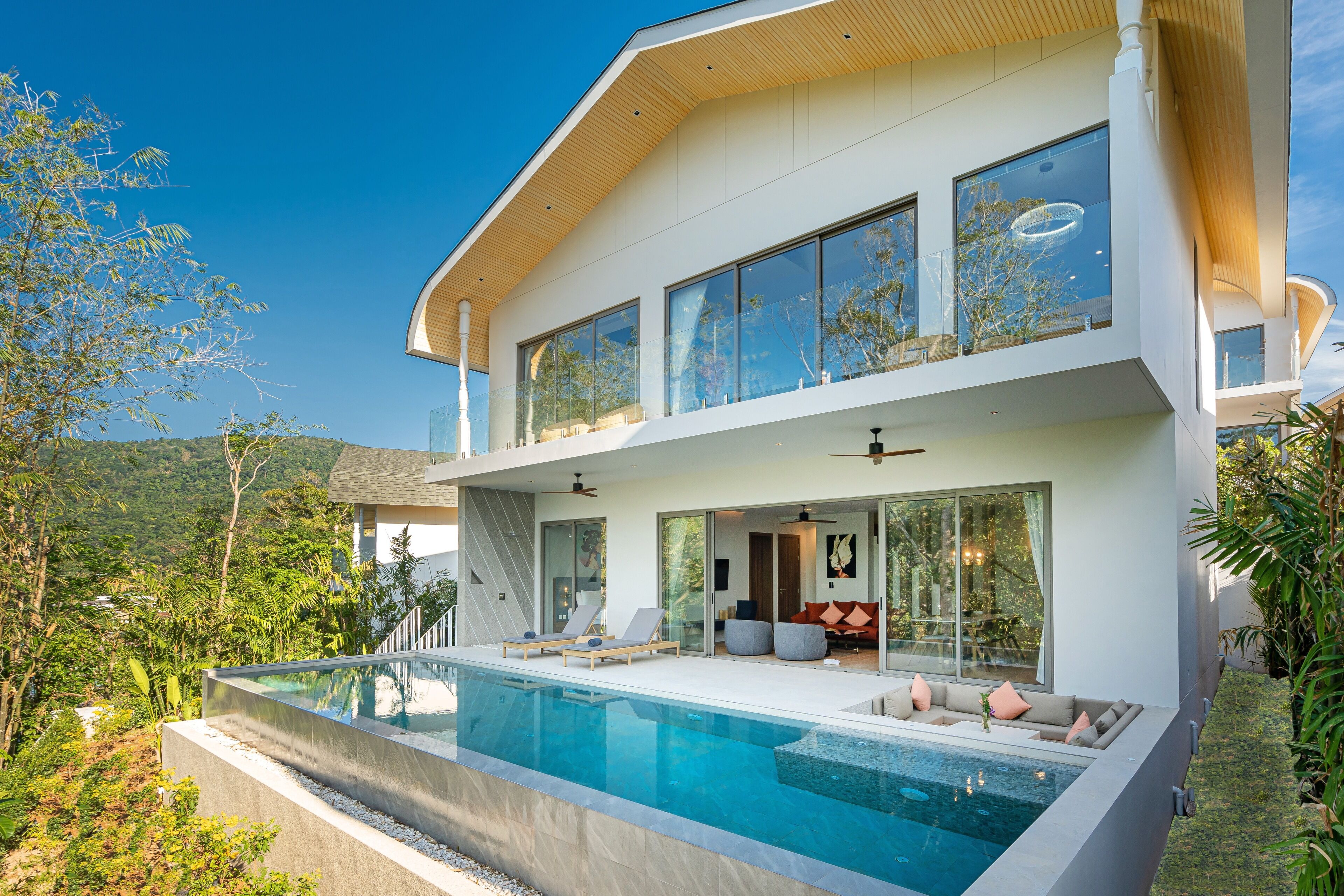 A modern two-story house with a large glass balcony, a swimming pool, and a lush garden.