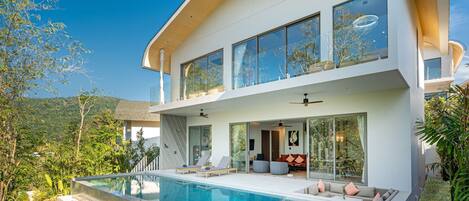 A modern two-story house with a large glass balcony, a swimming pool, and a lush garden.