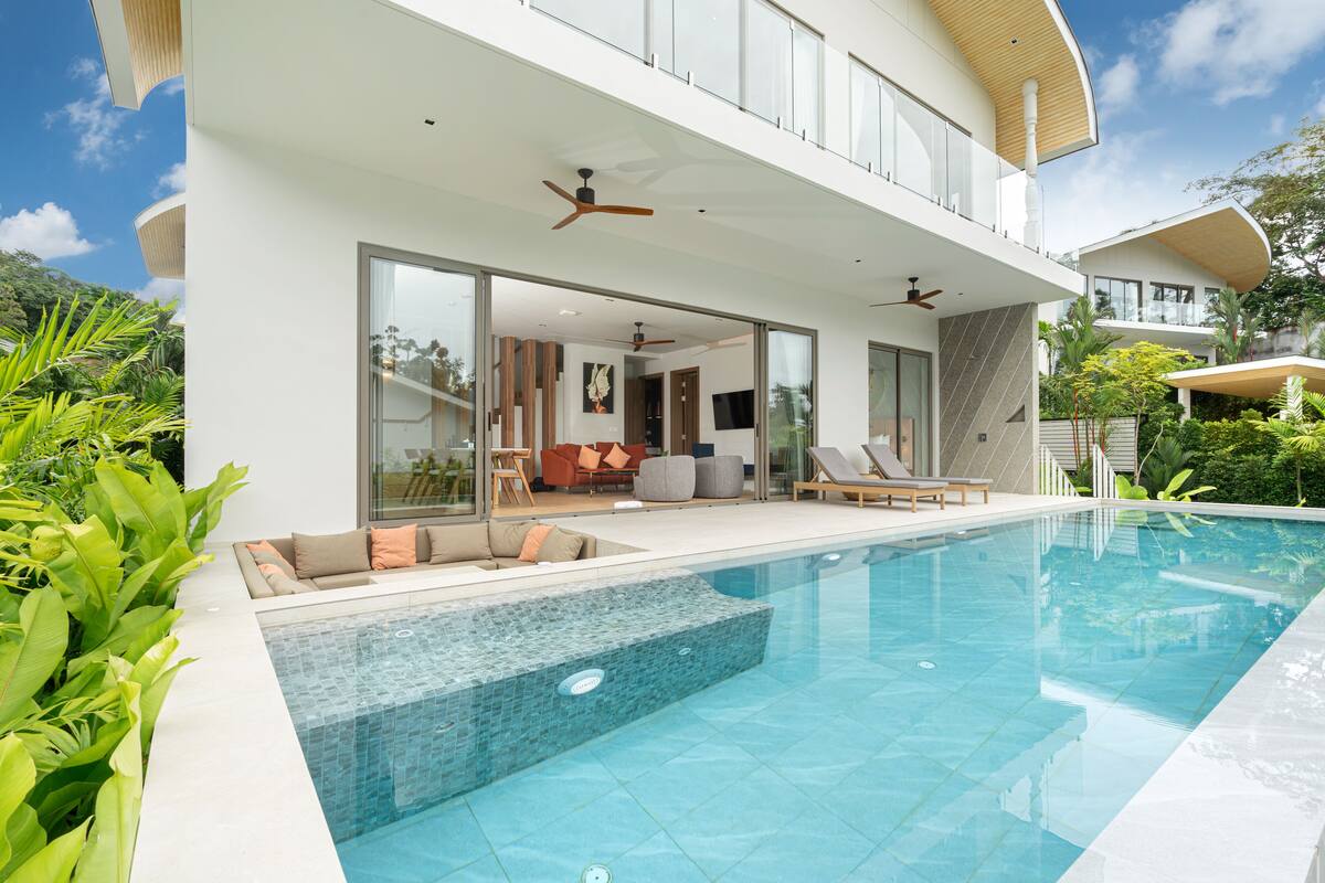 Une maison moderne dotée d’une piscine, de grandes fenêtres et d’un balcon.