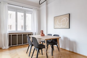 Uma sala de jantar com mesa de madeira, quatro cadeiras, um vaso e uma janela com cortinas brancas.