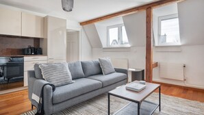 A modern apartment with a grey sofa, a small table, a kitchen area, and a view of the city through a window. - Trendy Unterstrass 2 Room w/ Storage, 10 min to Old Town, by Blueground (Zurich)