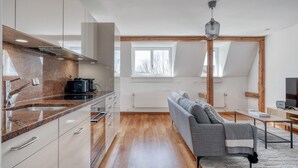A modern kitchen with granite countertops, a built-in oven, and a dining area with a gray sofa and a small table. - Trendy Unterstrass 2 Room w/ Storage, 10 min to Old Town, by Blueground (Zurich)