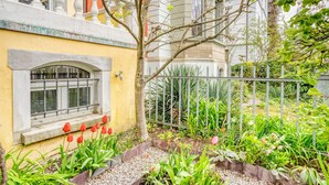A garden with a yellow wall, a window with a metal grill, and red tulips. - Trendy Unterstrass 2 Room w/ Storage, 10 min to Old Town, by Blueground (Zurich)
