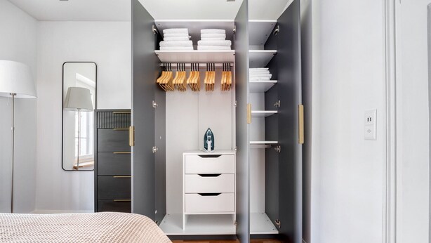 A modern bedroom with a bed, a wardrobe with hanging space for towels, and a mirror. - Trendy Unterstrass 2 Room w/ Storage, 10 min to Old Town, by Blueground (Zurich)