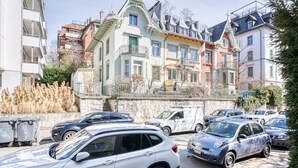 A row of colorful, multi-story buildings with balconies, parked cars, and a stone wall with dry plants. - Trendy Unterstrass 2 Room w/ Storage, 10 min to Old Town, by Blueground (Zurich)