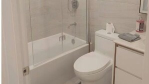 Un bany amb dutxa envidriada, un vàter blanc i un petit lavabo amb mirall.