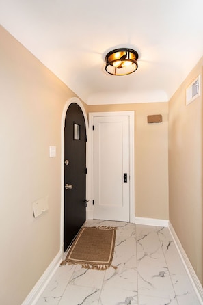 Stylish hallway with a door leading to a room, featuring a small rug and a ceiling light fixture.