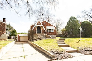 Situated on a well-maintained lawn, this charming home features a brick exterior and a pitched roof.