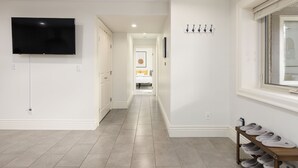 Un couloir avec un téléviseur fixé au mur, un meuble à chaussures et un lit visible au loin.