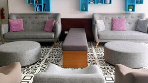 A modern living room with grey sofas, a central ottoman, and a blue shelving unit against a patterned wall. - Espacio Luxury- Edificio Pedro de Osma (Lima)