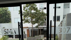 A modern building with a courtyard featuring a patterned floor, outdoor seating, and a tree. - Espacio Luxury- Edificio Pedro de Osma (Lima)
