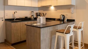 A modern kitchen with a central island, white bar stools, and a built-in oven. - Espacio Luxury- Edificio Pedro de Osma (Lima)