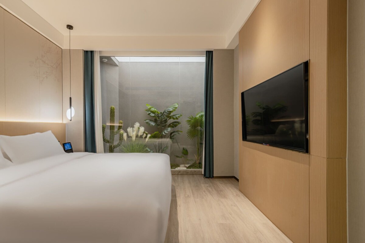 Habitación de hotel moderna con una cama grande, un televisor de pantalla plana montado en la pared y vistas a un jardín de cactus a través de una puerta de cristal.