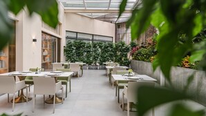 Ein Restaurant mit modernem Ambiente, das einen langen Essbereich mit Tischen und Stühlen, eine Glasdecke und einen grünen Hintergrund bietet.