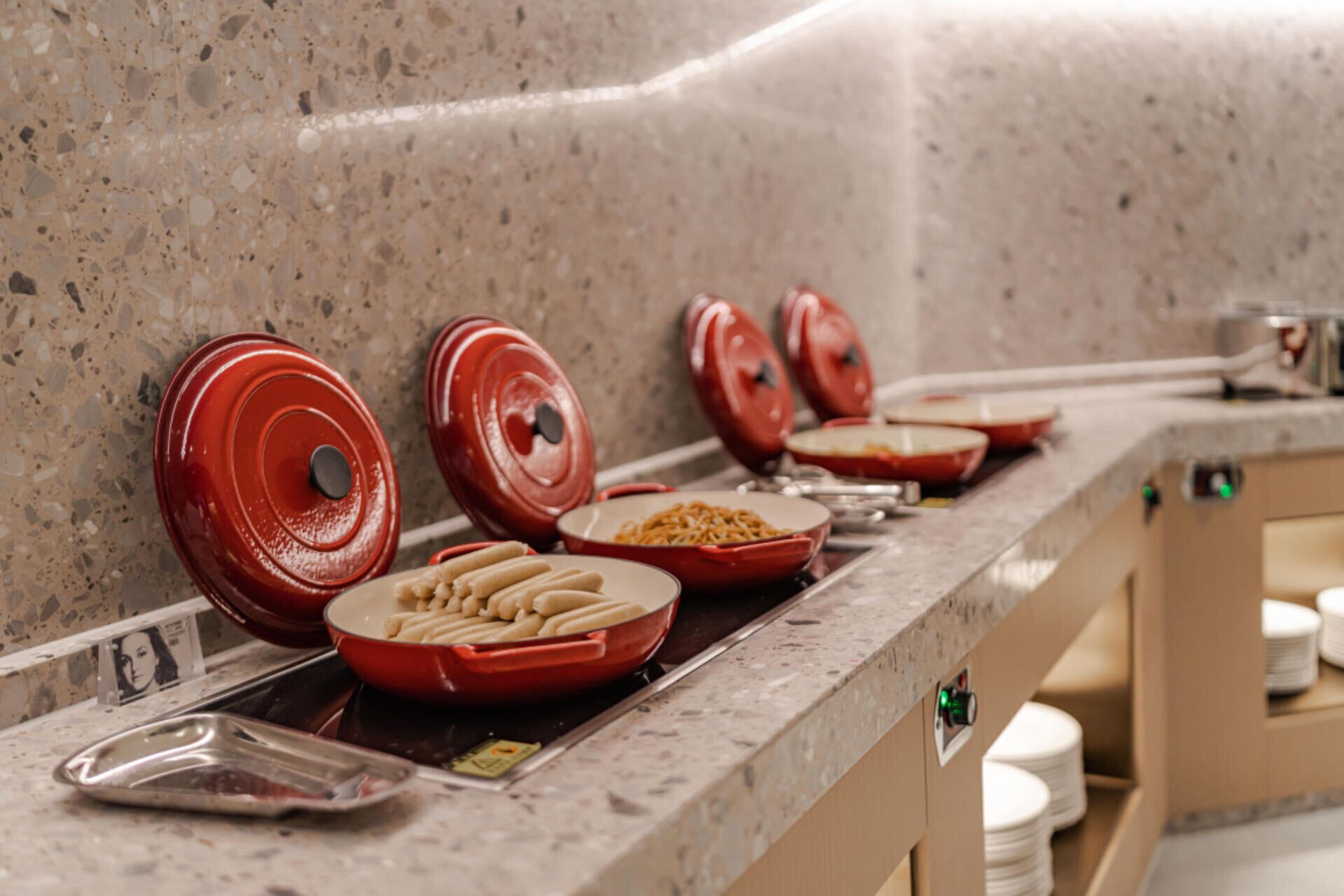 Una encimera de cocina con tapas rojas sobre diferentes platos, una bandeja con una fuente de galletas y una tarjeta con una imagen.