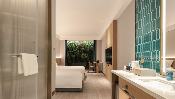 Ein modernes Hotelzimmer mit Bett, Schreibtisch, Badezimmer mit großem Spiegel und Blick ins Grüne.
