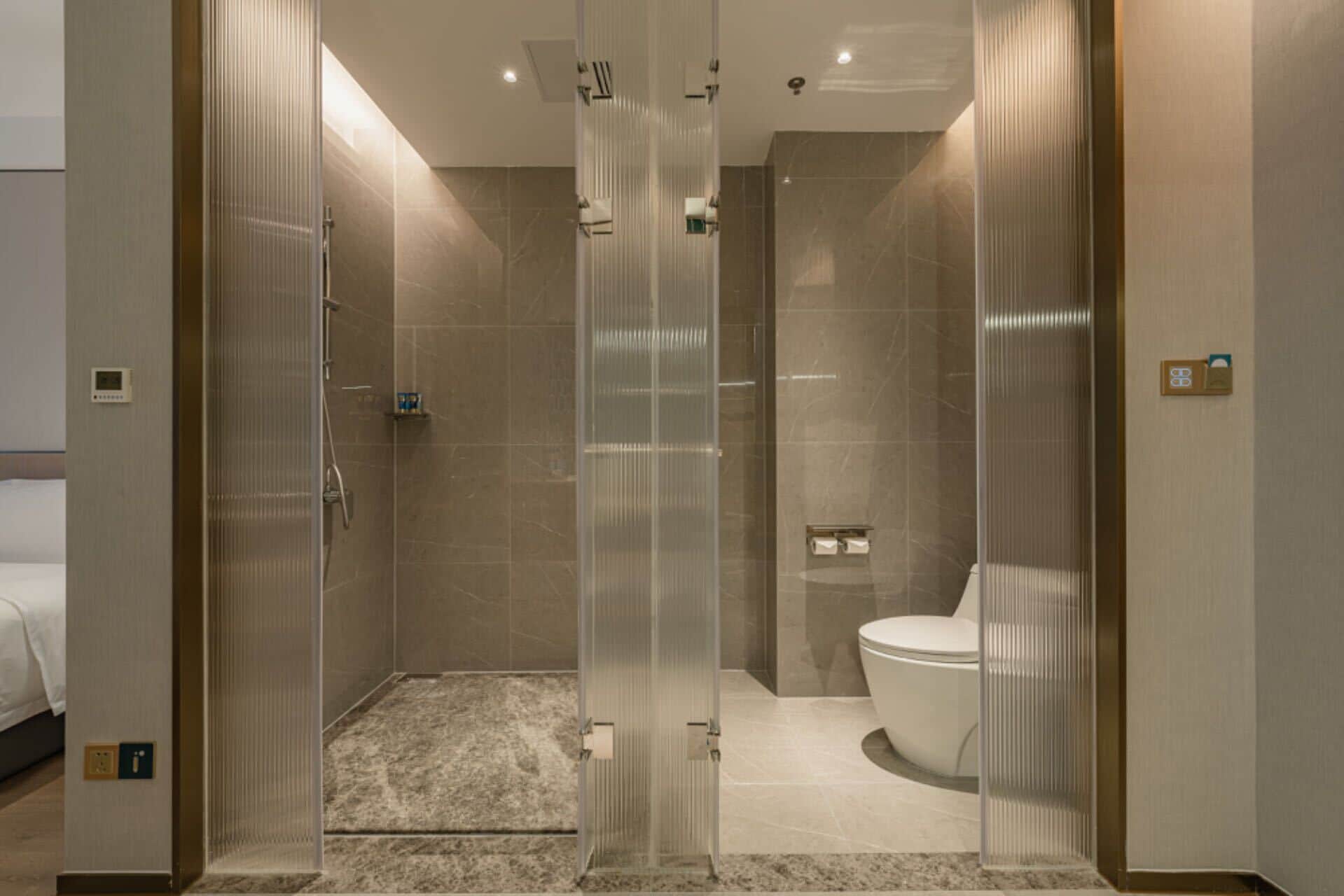 Une salle de bain moderne avec une douche à parois de verre, des toilettes et un lit dans la pièce adjacente.