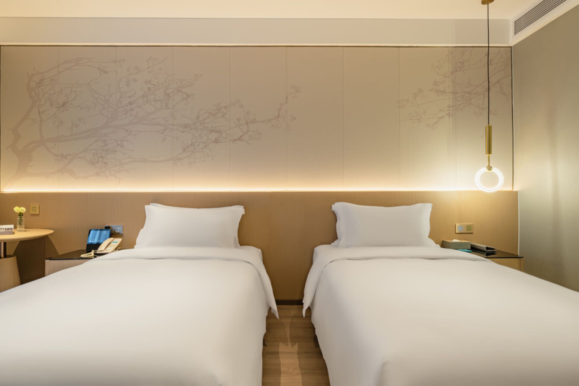 A hotel room with two beds, a desk with a phone, and a wall-mounted light fixture.