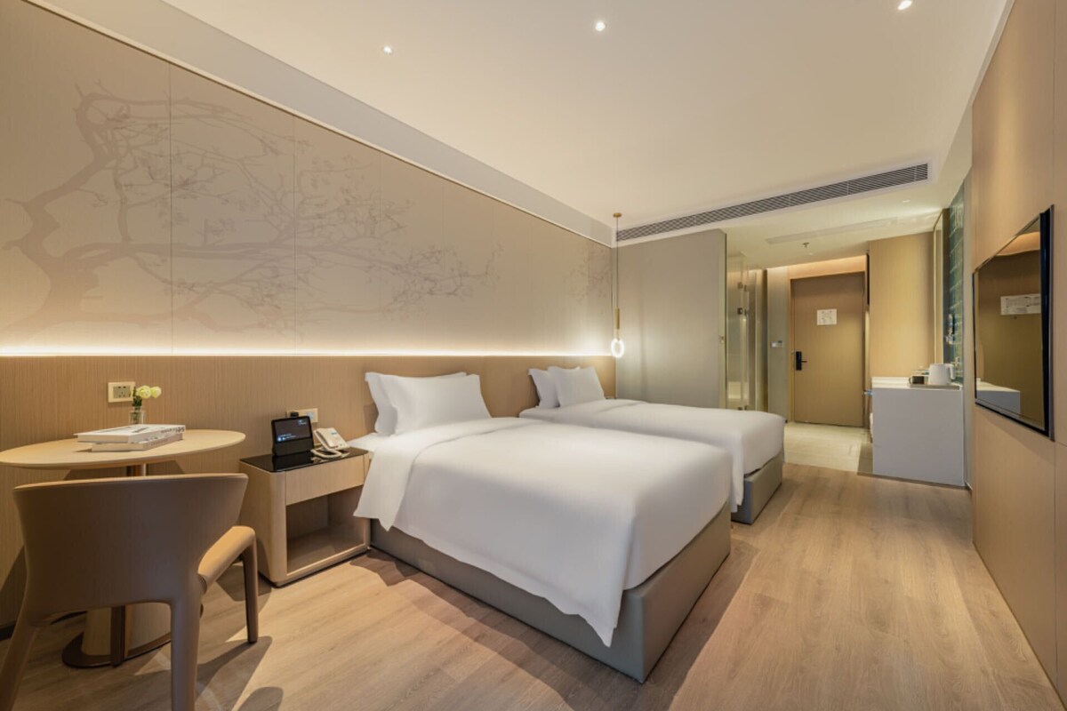 Ein Hotelzimmer mit zwei Betten, einem Schreibtisch, einem Sessel, einem runden Tisch und einem großen Spiegel.
