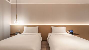 A hotel room with two single beds, a bedside table with a phone and a digital display, and a hanging light fixture.