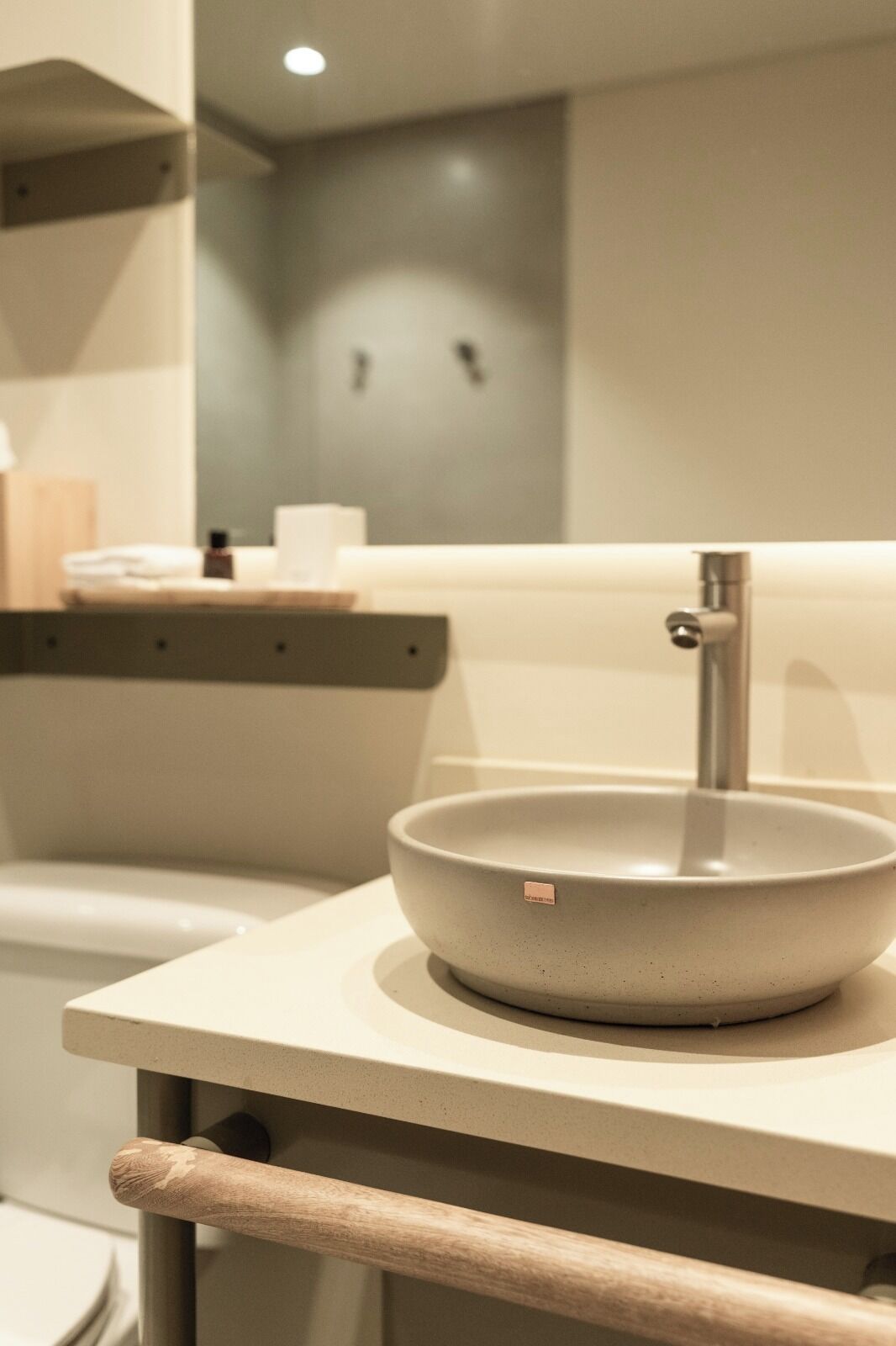 A modern bathroom with a round sink, a towel dispenser, and a mirror.
