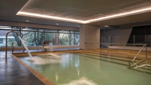 En swimmingpool med en fontän, stora fönster och en modern takdesign.
