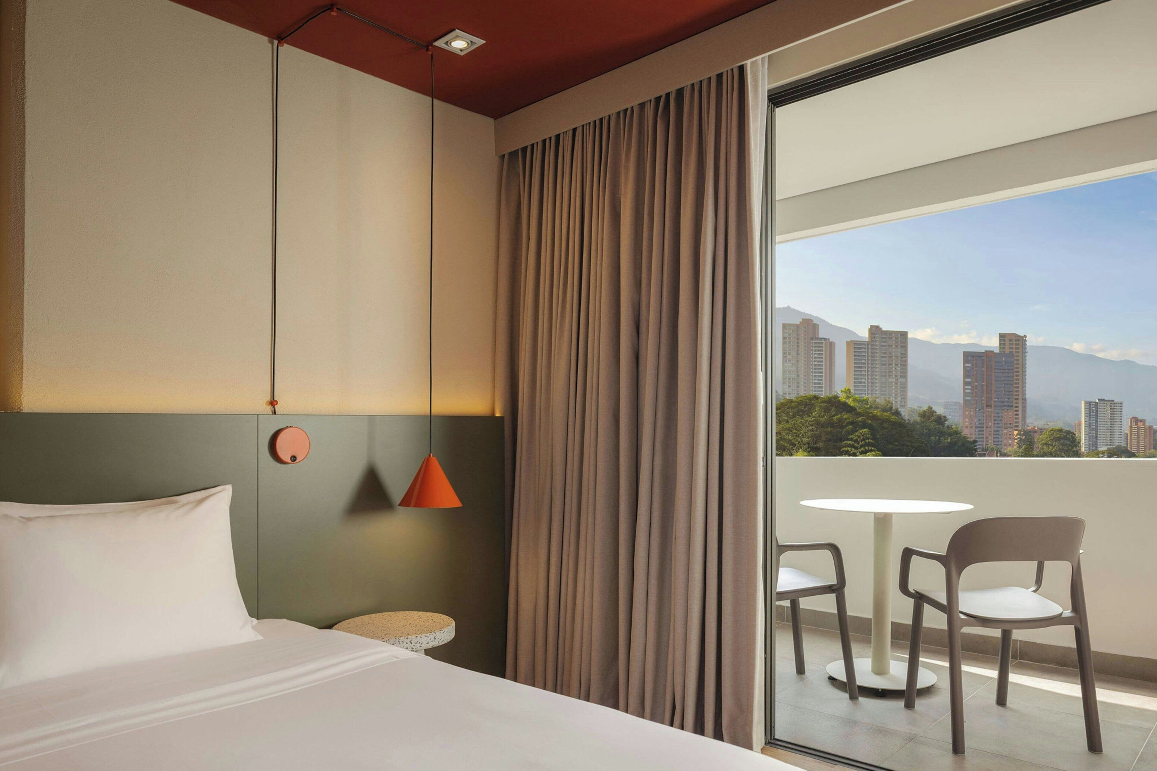 Une chambre d’hôtel avec un lit, une table ronde, deux chaises, une vue sur la ville et un rideau.