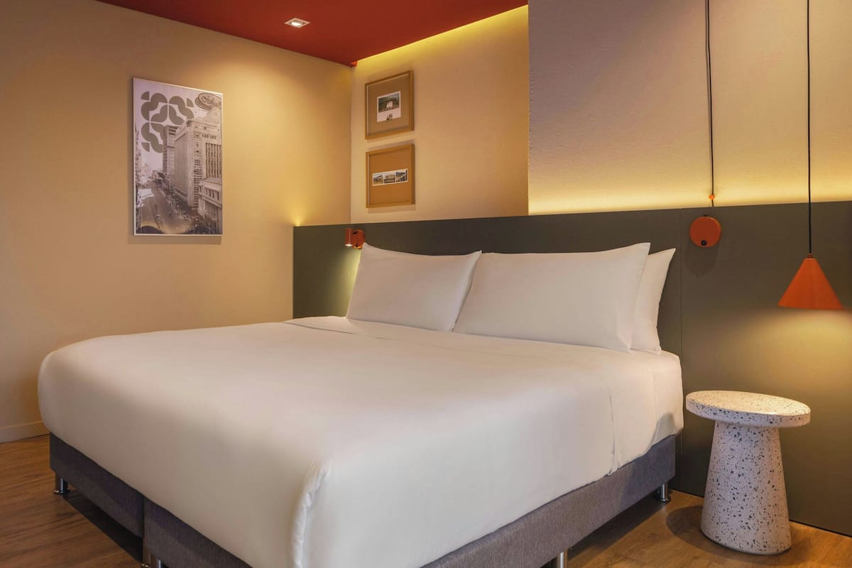Una habitación de hotel moderna con una cama grande, una mesita redonda pequeña y una lámpara de pared.