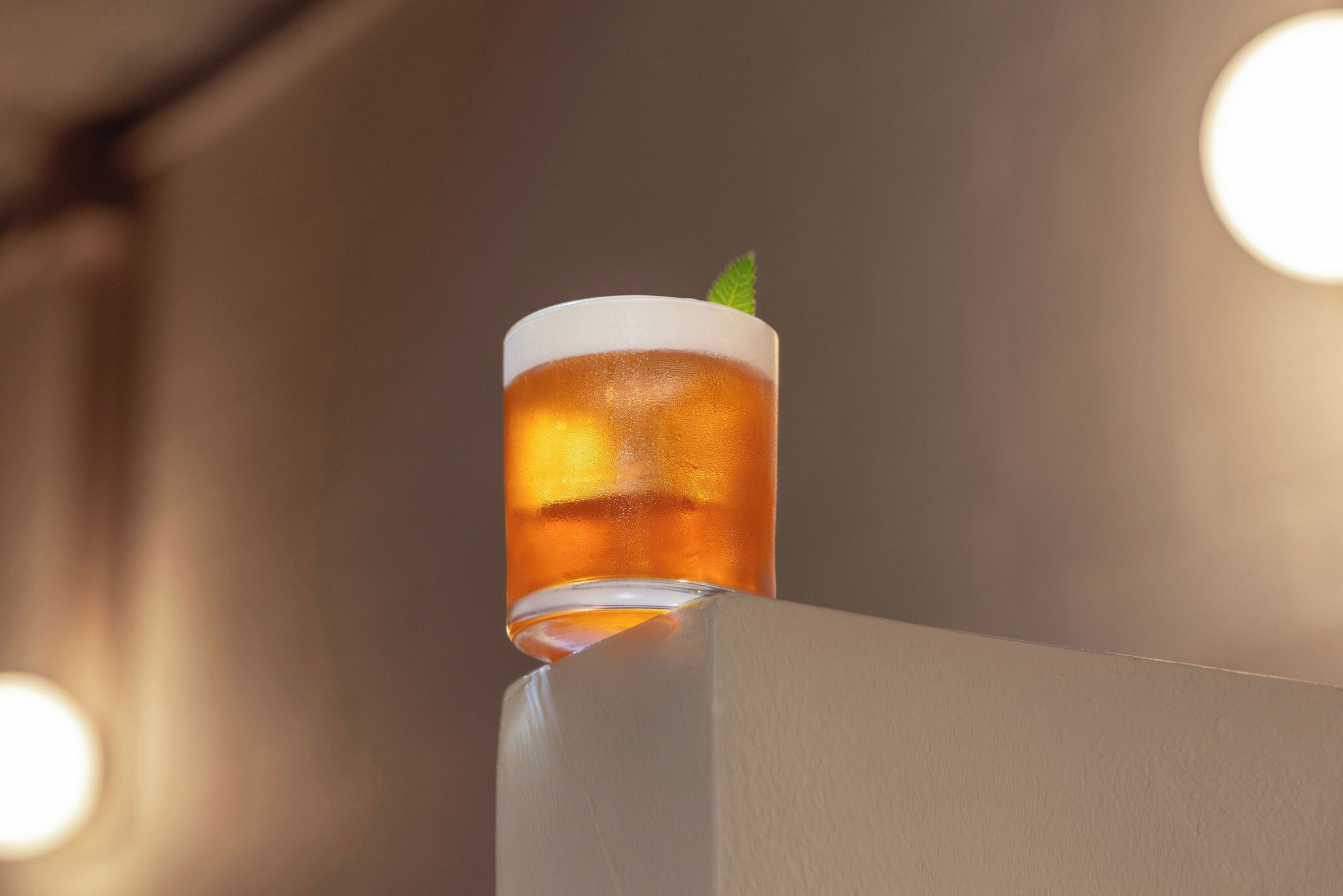 A glass of amber-colored beverage with ice cubes, placed on a white surface.