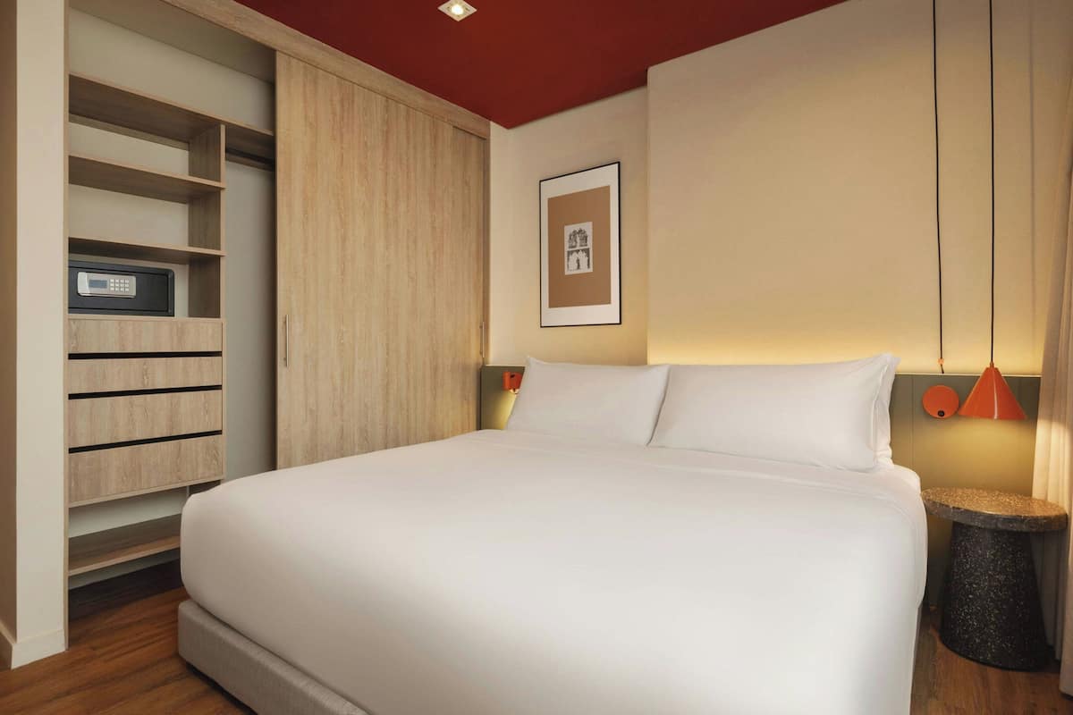 Un dormitorio con una cama, un armario, un cuadro en la pared y una mesita de noche con una lámpara.