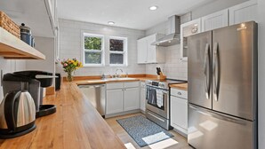 A modern kitchen with white cabinetry, stainless steel appliances, a wooden countertop, and a window with a view of trees. - Walk to Newport, 1st & 2nd Beaches, & Cliff Walk from this Newly Redone Home (Middletown)
