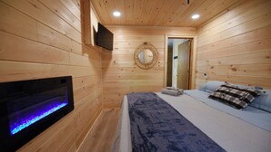 Un dormitorio de cabaña de madera con una cama, un televisor montado en la pared y un acuario integrado.