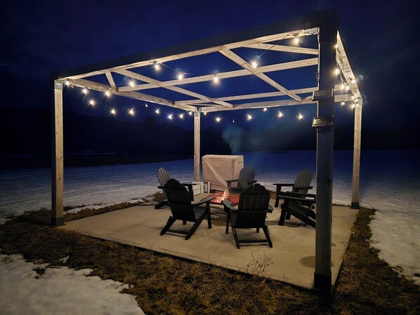 A covered outdoor seating area with chairs and a grill, overlooking a body of water.