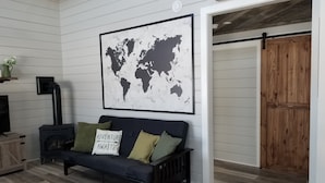 A cozy living room with a dark blue sofa, a world map on the wall, and a wooden door. - #5 Scenic Aspy Mountain Cottage, Margaree River access, near Cabot Trail (Margaree Valley)