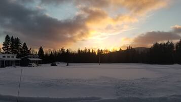Ett snötäckt fält med ett hus och träd i bakgrunden.