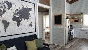 A modern living room with a world map, a dark sofa, and a kitchen with white cabinets and a wooden floor. - #5 Scenic Aspy Mountain Cottage, Margaree River access, near Cabot Trail (Margaree Valley)
