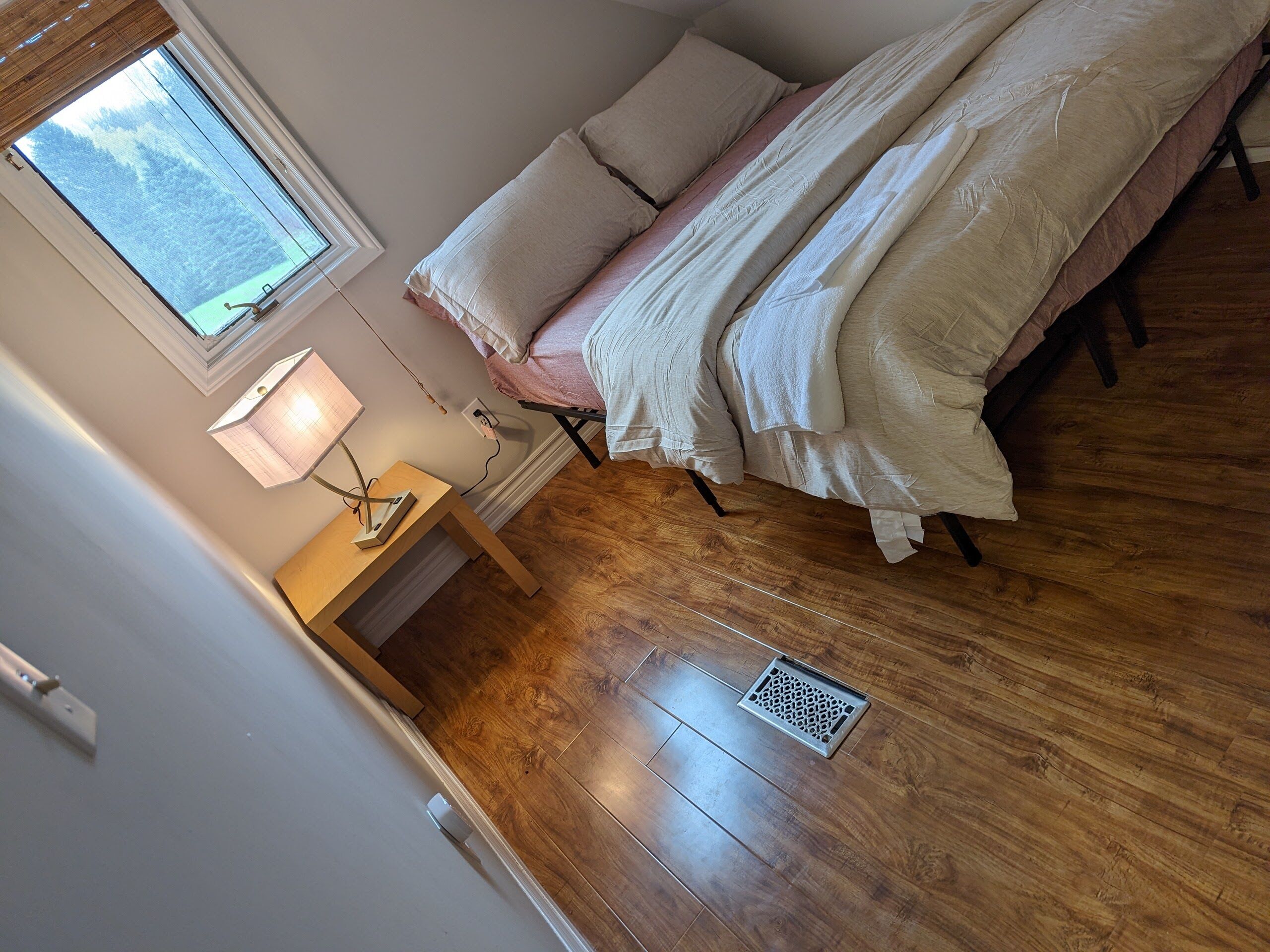 Ein Schlafzimmer mit Bett, Nachttisch, Lampe und einem Fenster mit Blick auf eine verschneite Landschaft.