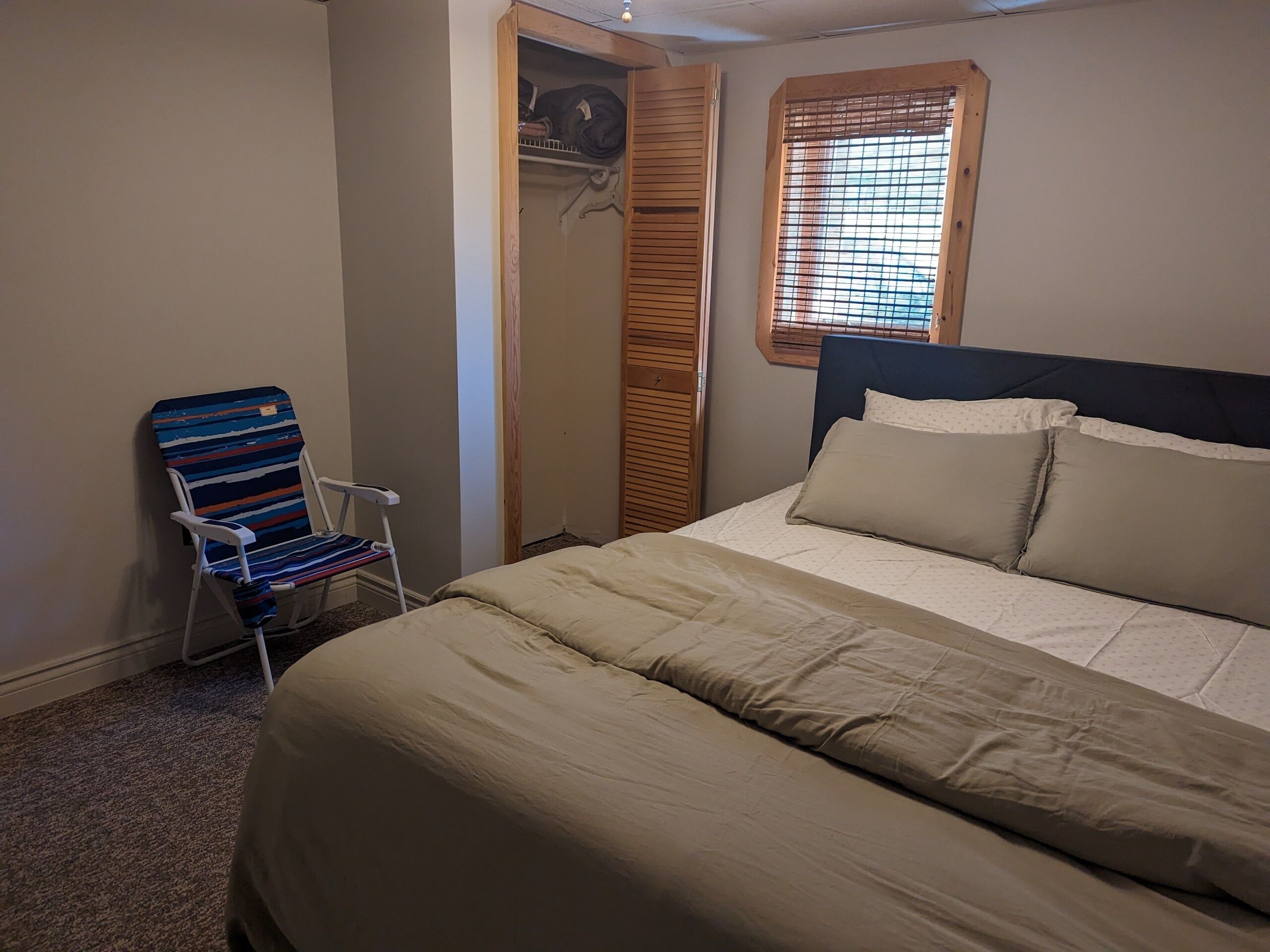 A bedroom with a bed, a chair, a wardrobe, and a window with blinds.