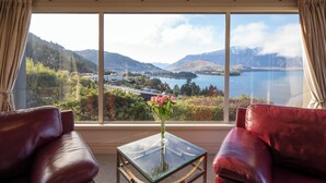 A room with a large window offering a view of a lake and mountains. There is a glass table with a vase of flowers in the center. - Aspen House (Queenstown)