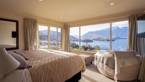 A spacious bedroom with a large bed, a seating area, and a view of mountains and a lake. - Aspen House (Queenstown)