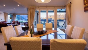 A dining area with a glass table, cushioned chairs, a decorative pinecone centerpiece, and a view of mountains through large windows. - Aspen House (Queenstown)
