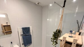 Un baño moderno con cabina de ducha de vidrio, un lavamanos blanco y suelo de madera.
