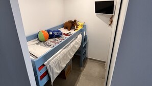 Una habitación pequeña con una cama individual azul, un escritorio y un televisor montado en la pared.