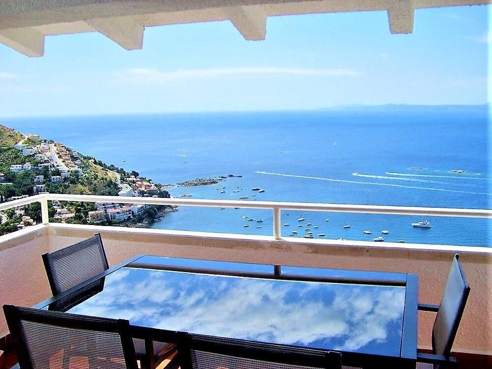 Un balcone con tavolo e sedie che si affaccia su una vista costiera con barche e una costa in lontananza.