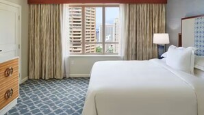 A hotel room with a large bed, a dresser, a window with curtains, and a view of buildings. - Grand Waikikian 1BR Partial Oceanview Villa (Kapolei)