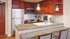 A kitchen with wooden cabinets, stainless steel appliances, granite countertops, and pendant lighting. - Grand Waikikian 1BR Partial Oceanview Villa (Kapolei)